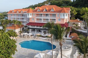 A large hotel with multiple balconies, a swimming pool, and palm trees.