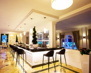 A bar area with a marble floor, bar stools, a large potted plant, and a view of the outside.