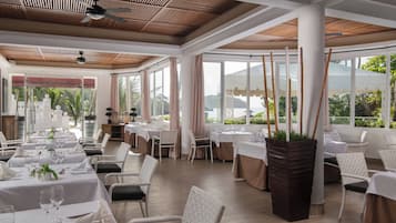 Un restaurant doté de nombreuses tables et chaises, de grandes fenêtres et d’un ventilateur de plafond.