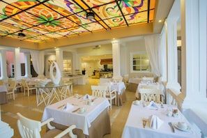 A spacious dining area with round tables, white chairs, and a colorful stained glass ceiling. - Bahia Principe Escape Samaná Hyatt Incl Co Adult O (Samaná)