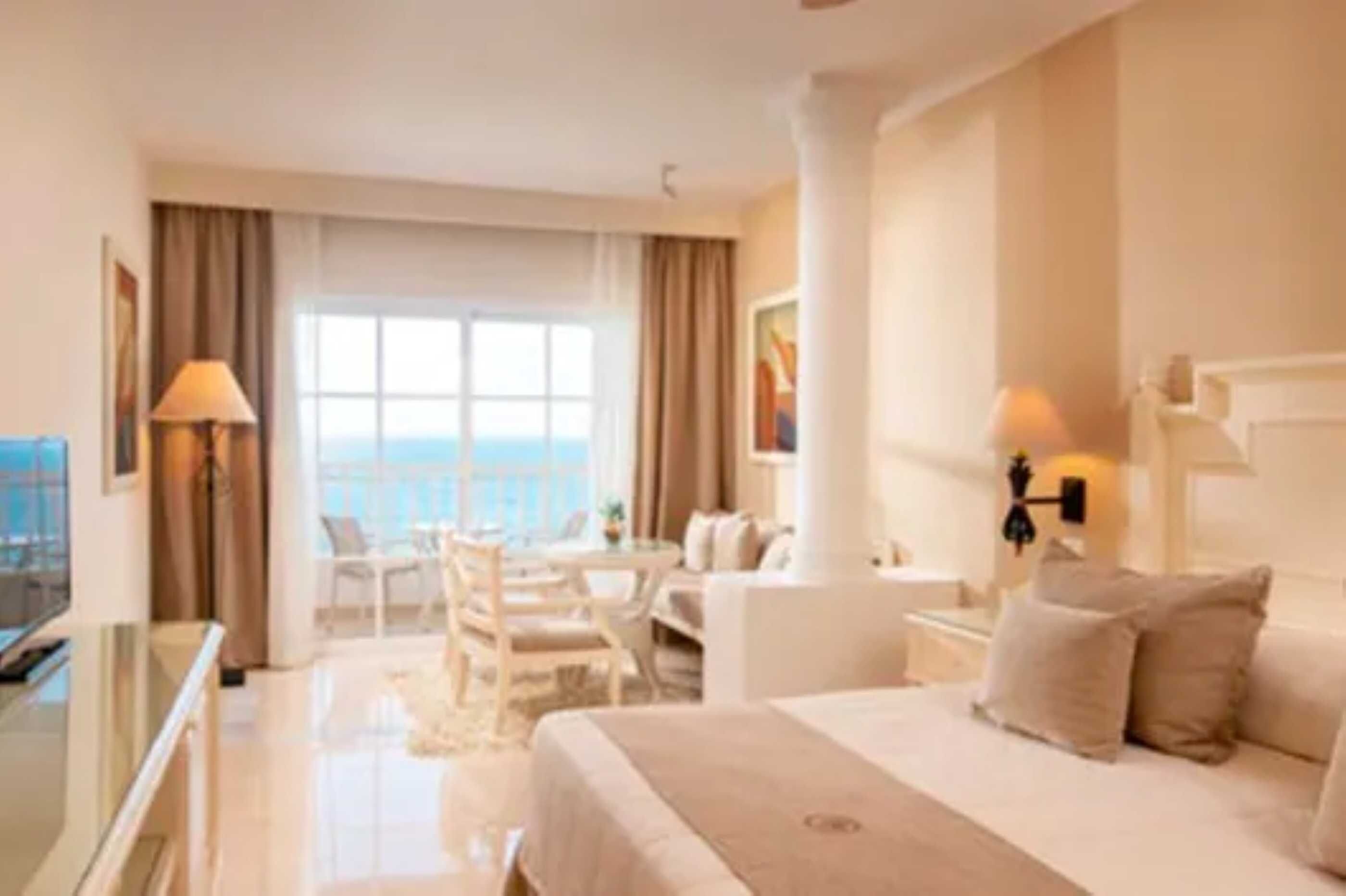 A hotel room with a bed, a desk, a chair, and a view of the sea.