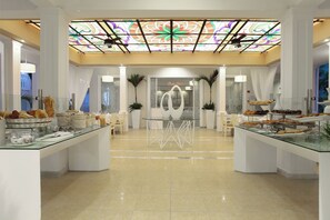 Un vestíbulo de hotel con una barra de café de vidrio, una recepción y un techo decorativo.