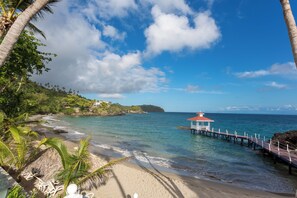 A beach with a pier extending into the ocean, palm trees, and a small structure on the pier.