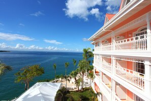 A hotel with a balcony overlooking a body of water, palm trees, and a clear sky.