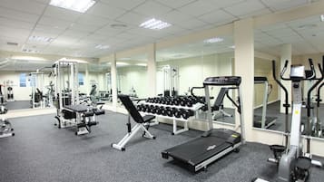 Une salle de sport équipée de machines d’exercice, de miroirs et d’un tapis de course.