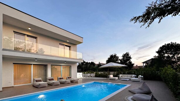 Ein modernes, zweistöckiges Haus mit Swimmingpool, Sitzgelegenheiten im Freien und einer überdachten Terrasse.