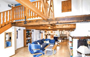 Ein geräumiger Wohnbereich mit einer Holztreppe, einer Küche im Hintergrund und einem Essbereich mit Tisch und Stühlen.