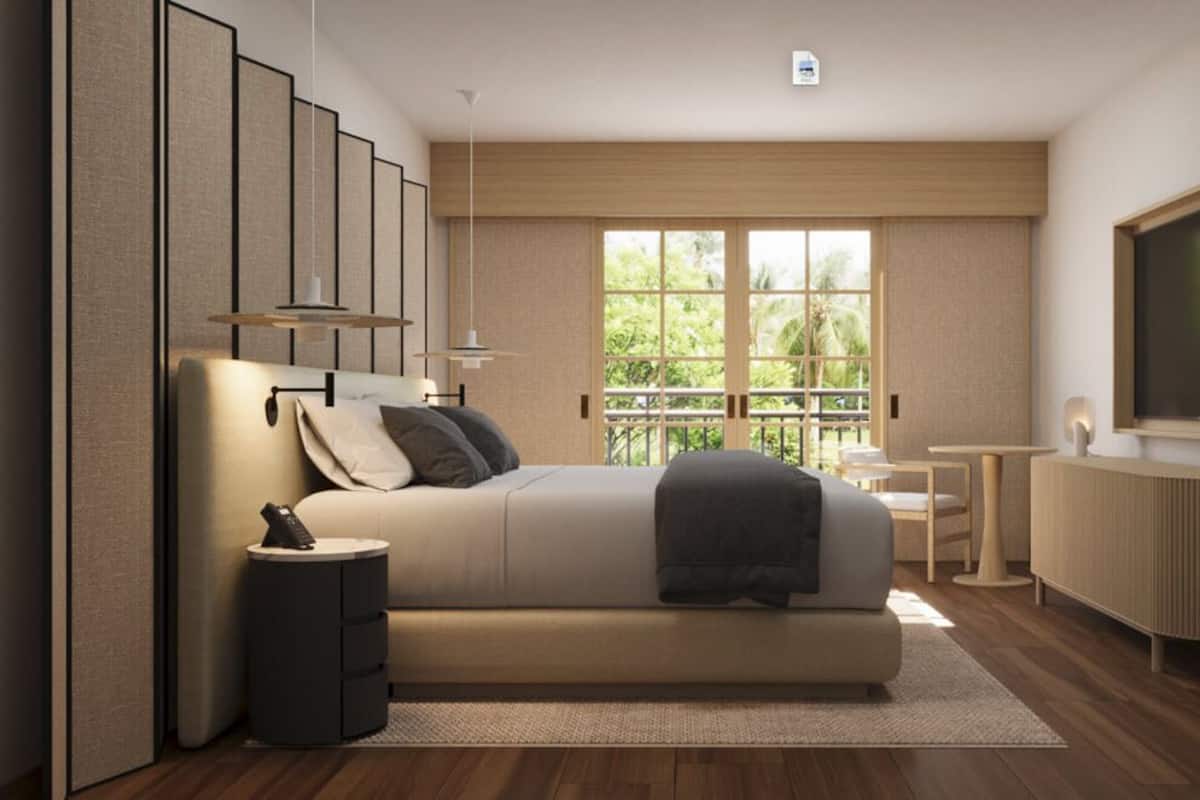 A modern bedroom with a sofa bed, a small table, a TV, and a view of greenery through large windows.