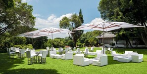 Un espace extérieur aménagé avec des meubles blancs et des parasols, entouré de verdure et d’arbres.
