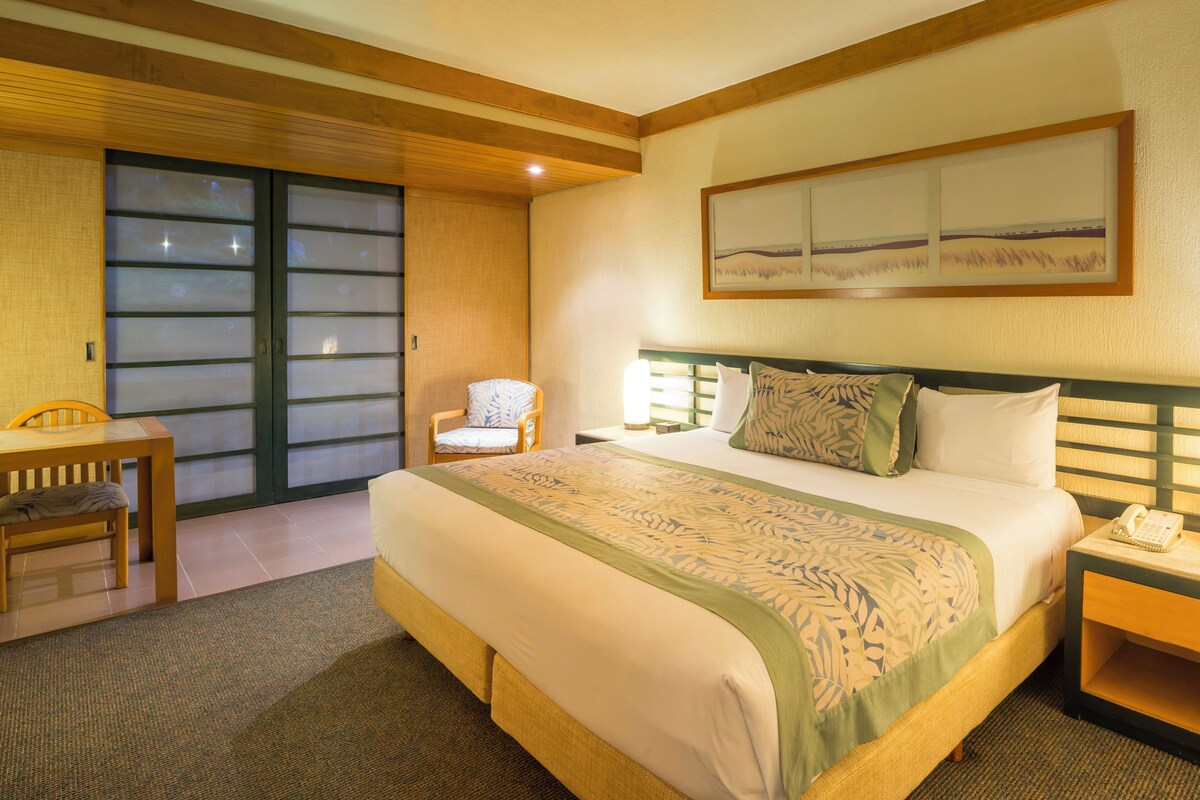 Une chambre d’hôtel avec un lit, une chaise, un bureau et une table de chevet avec une lampe.