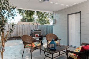 Une terrasse extérieure avec des chaises en osier, une table, une lanterne et un barbecue.