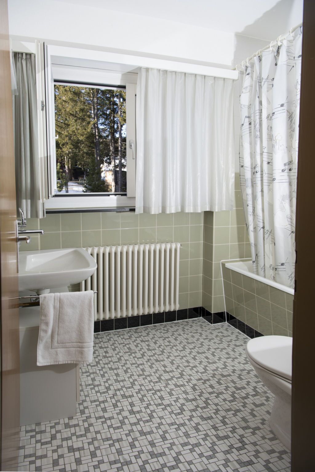 A bathroom with a window, a radiator, a sink, a toilet, and a shower curtain.