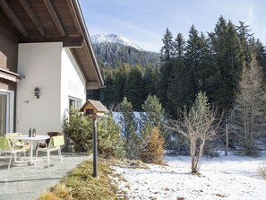 Un edificio con un patio, una terraza de madera y vistas a montañas y árboles cubiertos de nieve.