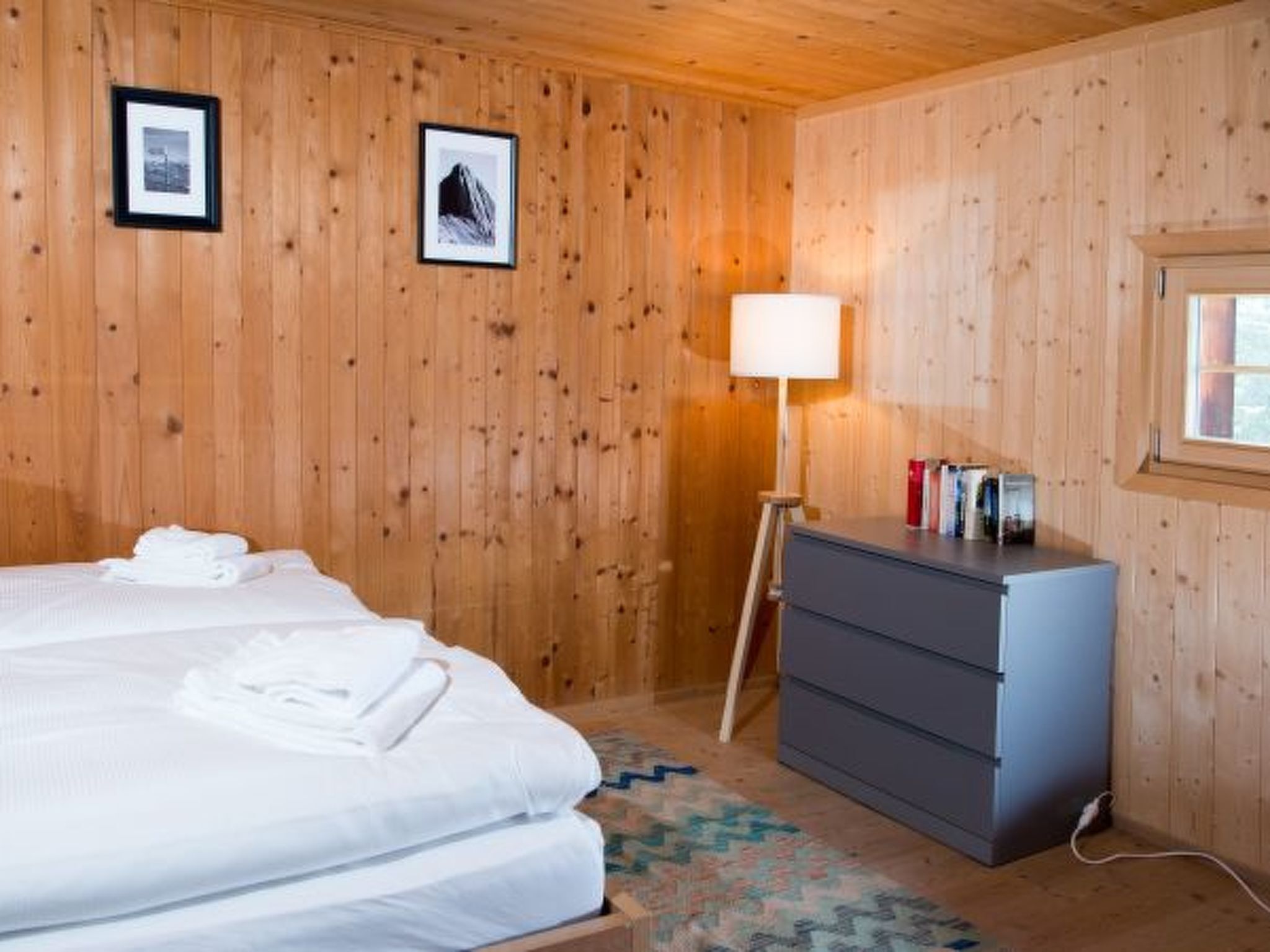 Een kamer met houten lambrisering, een bed, een dressoir, een lamp en ingelijste foto's aan de muur.