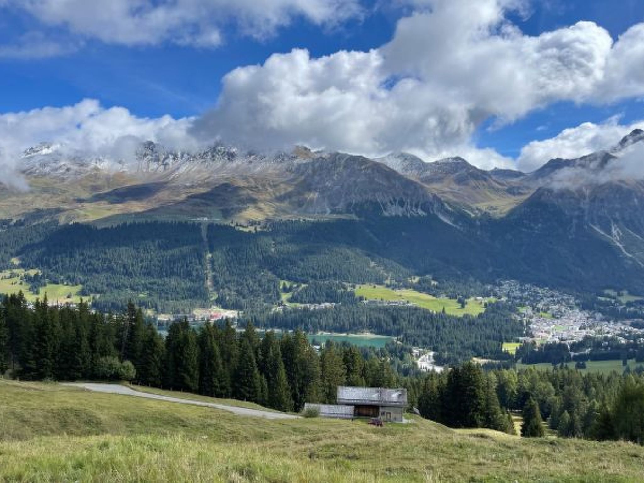 A mountainous landscape with a small building in the foreground, surrounded by dense forests and a town in the valley below.