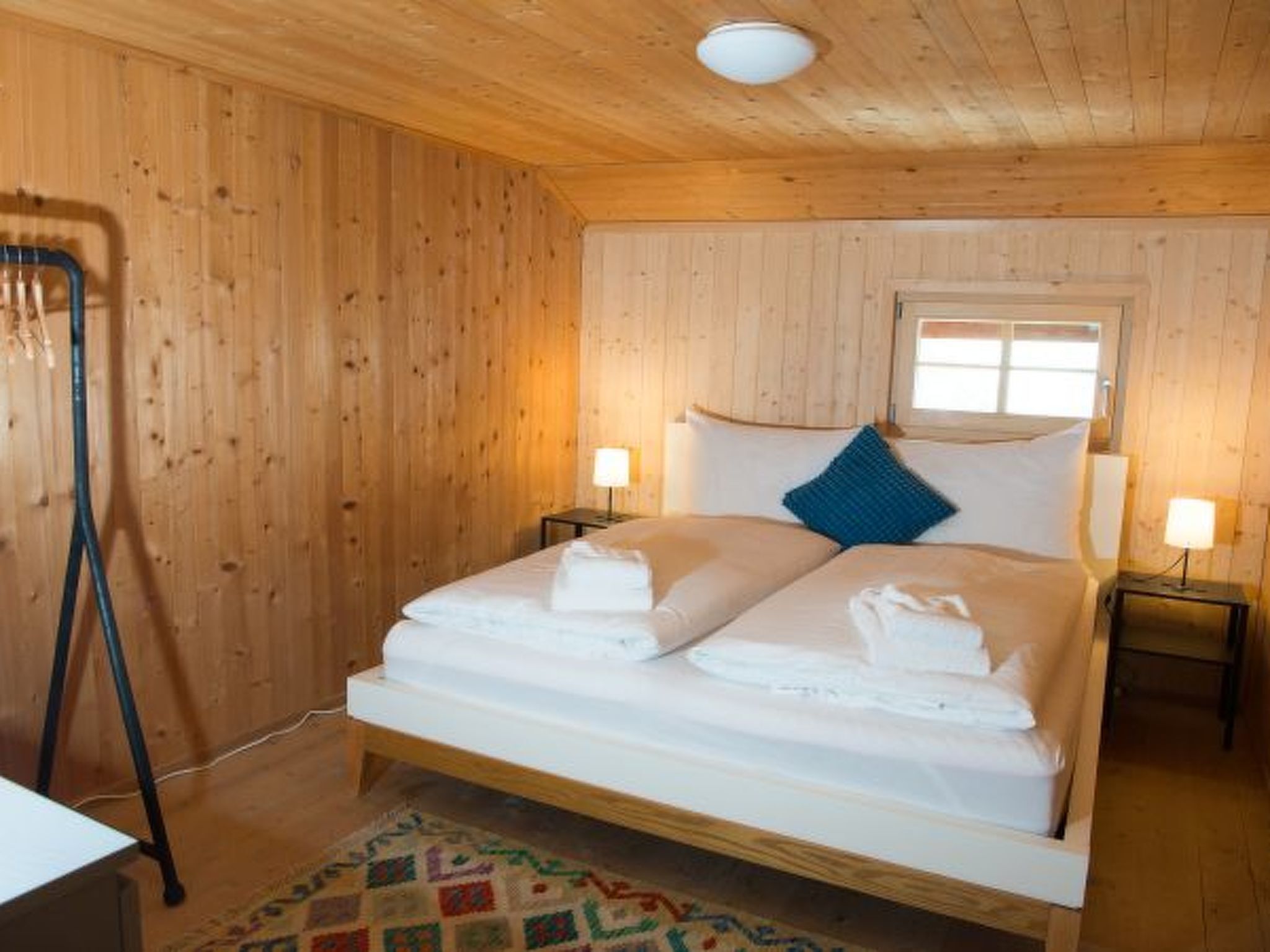 Ein Zimmer mit Holzwänden, einem Bett, zwei Nachttischlampen und einem Fenster.
