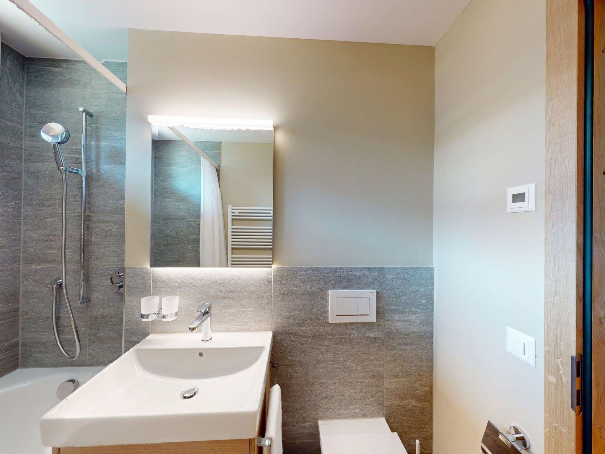 A modern bathroom with a large mirror, a sink, a shower, and a towel rack.