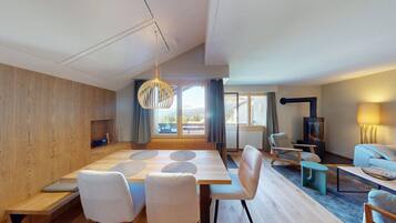 Ein modernes Wohnzimmer mit Holzboden, einem Esstisch mit Stühlen, einer Couch, einem Fernseher und einem Kamin.