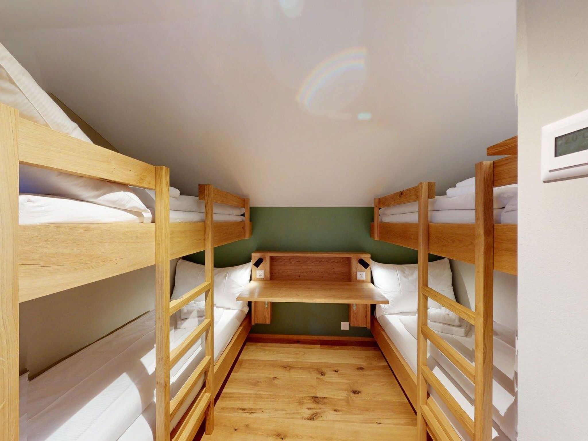 Habitació amb un llit superposat, escriptori i termòstat fixat a la paret.