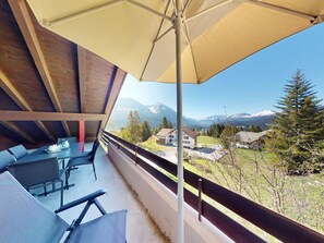 A balcony with a table and chairs, a large umbrella, and a view of mountains and houses. - 1510 Chesa Barlangia Briza by Interhome (Valbella)