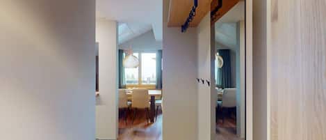 A modern interior with a wooden floor, a dining area with chairs and a table, and a view through a doorway.