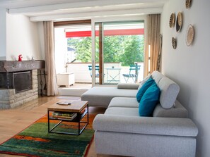 Una sala de estar moderna con chimenea, un sofá con cojines azules, una mesa de centro y vistas al exterior a través de grandes puertas de vidrio.