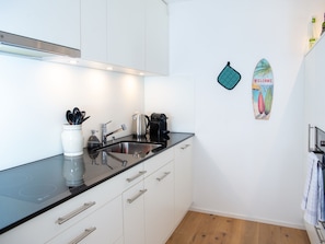 A modern kitchen with white cabinets, a black countertop, and a stainless steel sink. There is a kettle, a coffee maker, and a toaster on the counter. - 1614 La Riva 401 by Interhome (Lenzerheide)