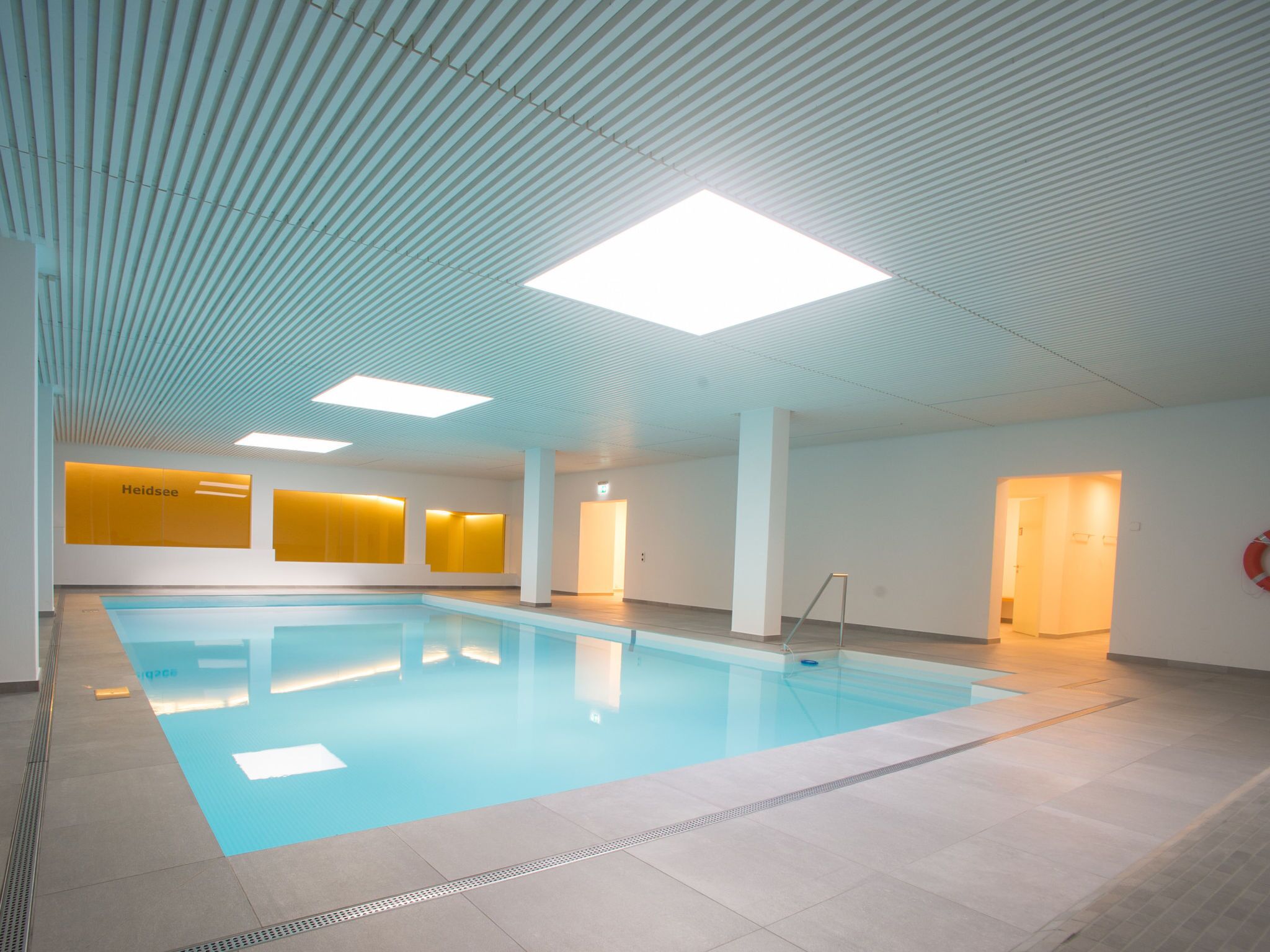 Una piscina interior con suelo de baldosas, techo con diseños lineales y una luminaria brillante.