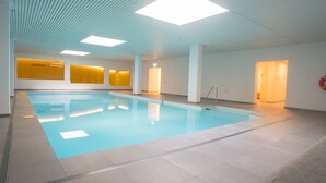 Piscina interna com chão ladrilhado, teto com padrões lineares e luminária clara.