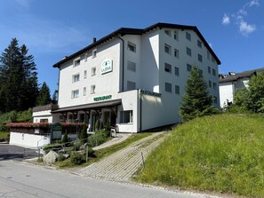 Un immeuble à plusieurs étages, avec un restaurant au rez-de-chaussée, entouré de verdure et d’arbres.