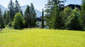 A grassy field with a building in the background surrounded by trees and mountains.