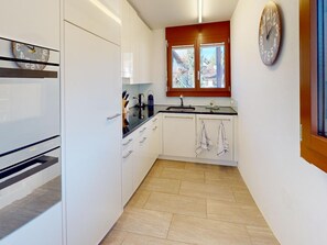 A compact kitchen with white cabinetry, a built-in oven, a window with a view, and a wall clock. - 1905 Tgampi Sot Lantsch/Lenz by Interhome (Lantsch)