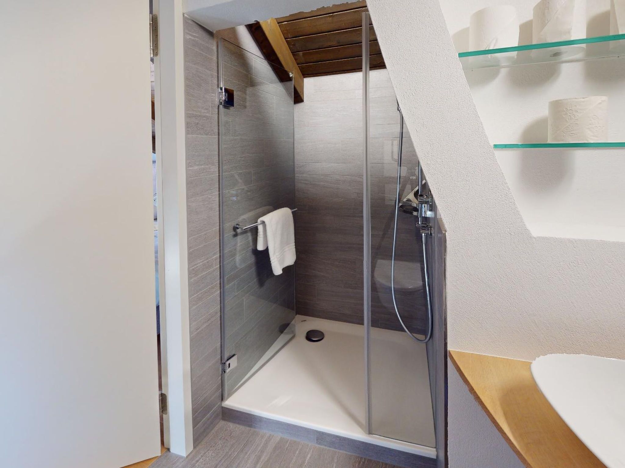 Ein modernes Badezimmer mit einer Duschkabine aus Glas, einem weißen Waschbecken und einer Glasablage für Toilettenartikel.