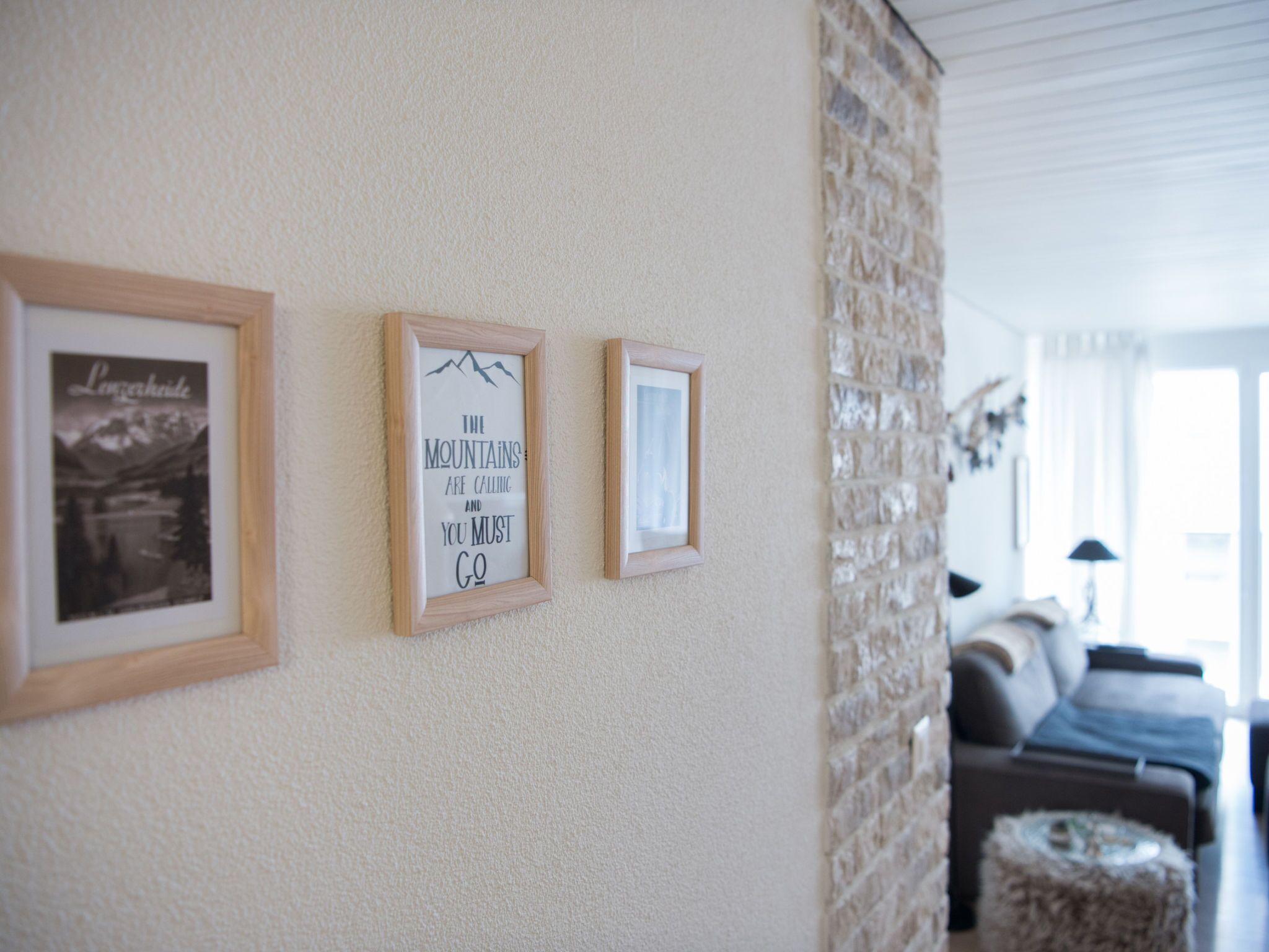 Una pared con tres cuadros enmarcados, pared de piedra y un salón con sofá y reposapiés.