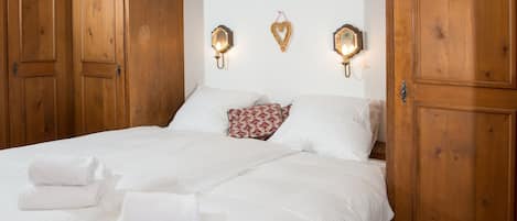 Cama doble con sábanas blancas y dos almohadas, una decoración de pared con forma de corazón y dos lámparas de pared.