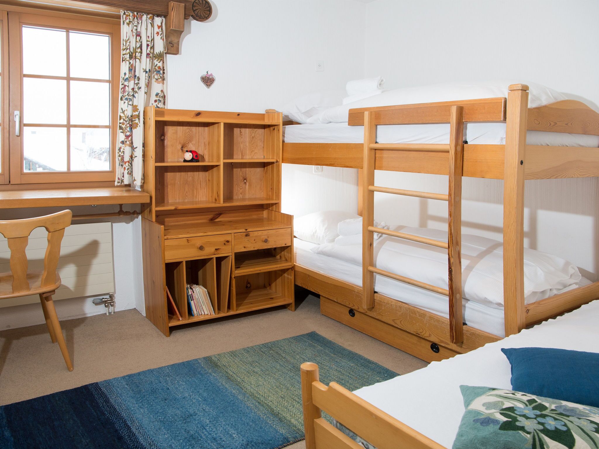 A room with bunk beds, a desk with a chair, and a window with curtains.