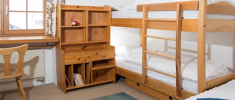 A room with bunk beds, a desk with a chair, and a window with curtains.