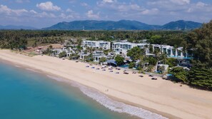 Een strandresort met meerdere gebouwen, een zandstrand en een uitzicht op verre bergen.
