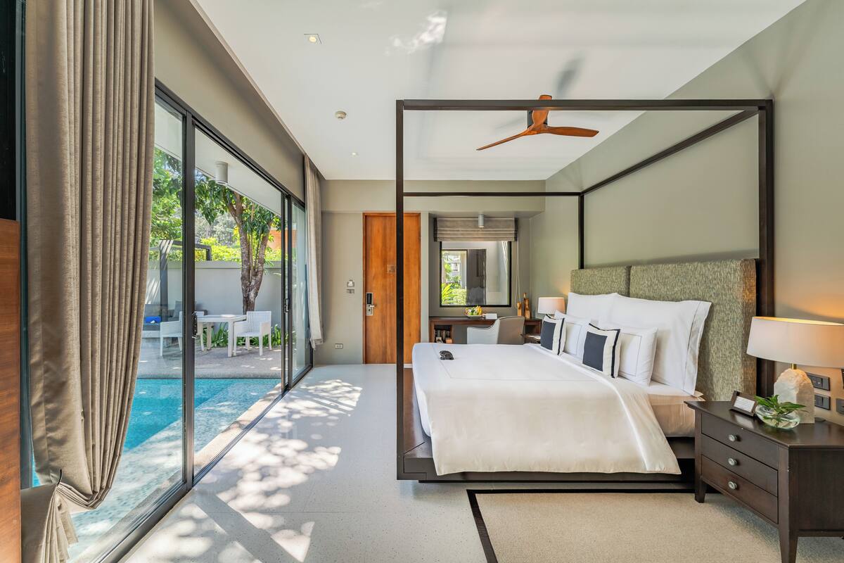 A modern hotel room with a large bed, a ceiling fan, a desk, and a view of a swimming pool.