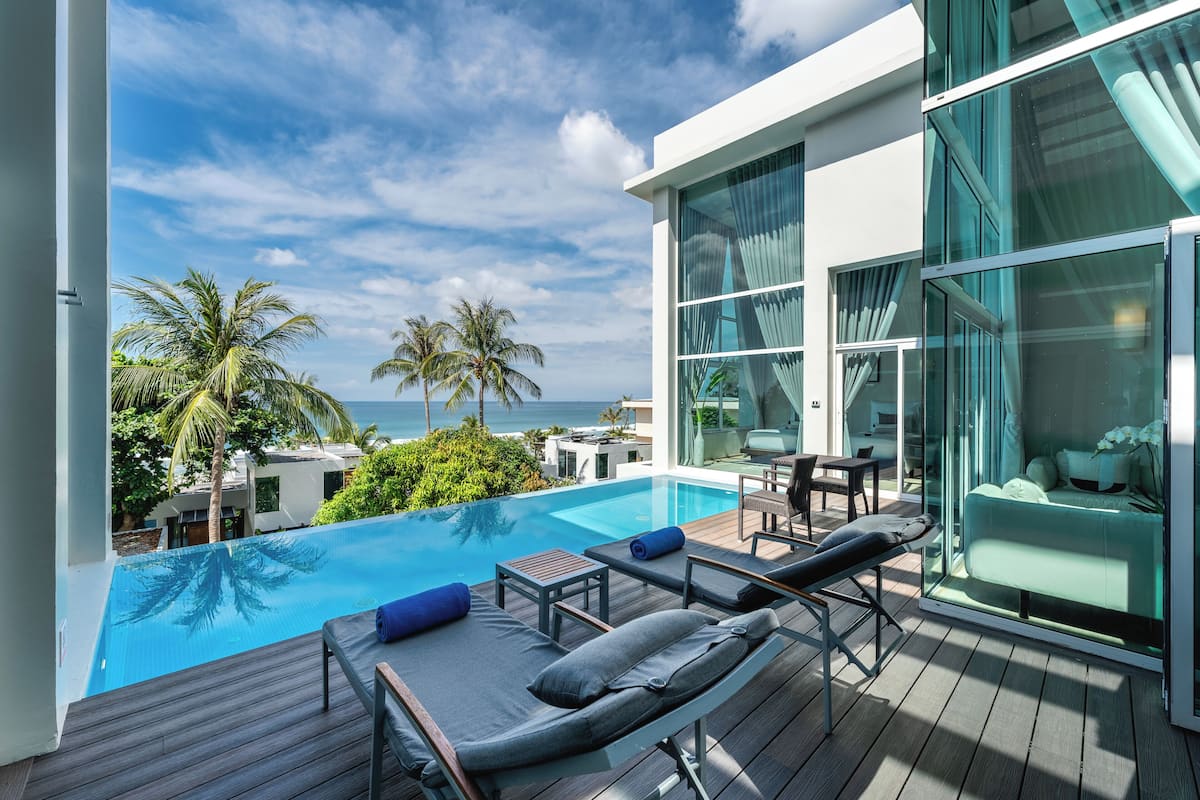 A modern hotel with a pool, lounge chairs, and a view of the ocean.