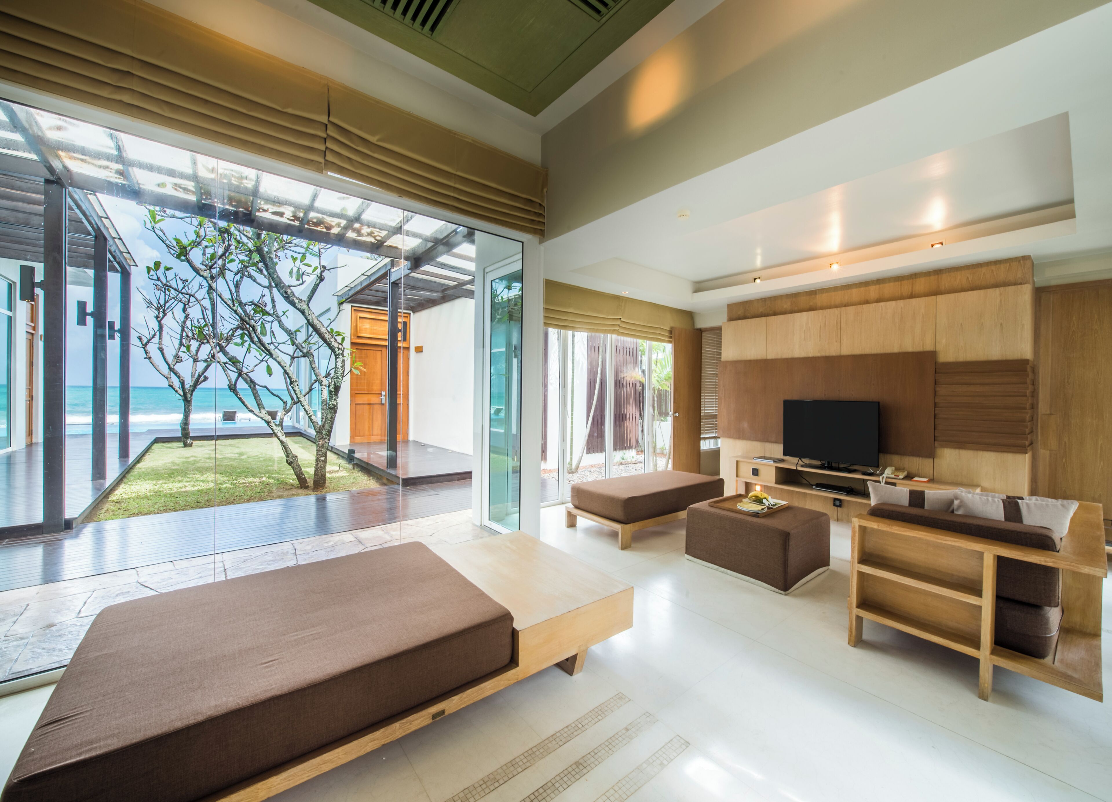 Ein modernes Wohnzimmer mit großem Fernseher, Holzmöbeln und einer Glastür, die auf einen Balkon mit Meerblick führt.