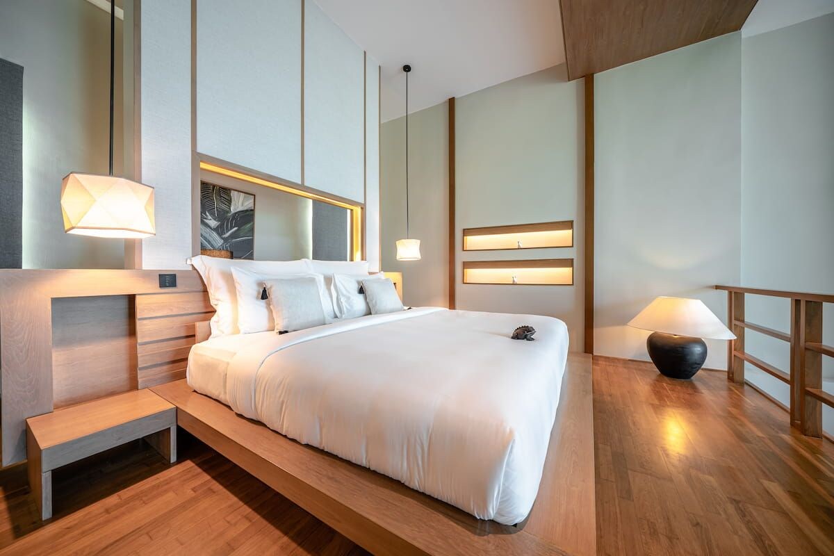 Quarto de hotel moderno com uma cama grande, mesas de cabeceira e vista para a cidade.