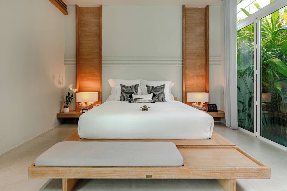 A modern bedroom with a large bed, bedside tables, and a view of greenery through a large window.