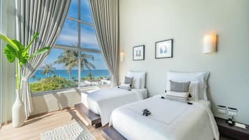A hotel room with two beds, a large window with curtains, a plant, and a view of the ocean.