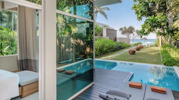 A modern pool area with a glass wall, a wooden deck, and a view of the ocean.