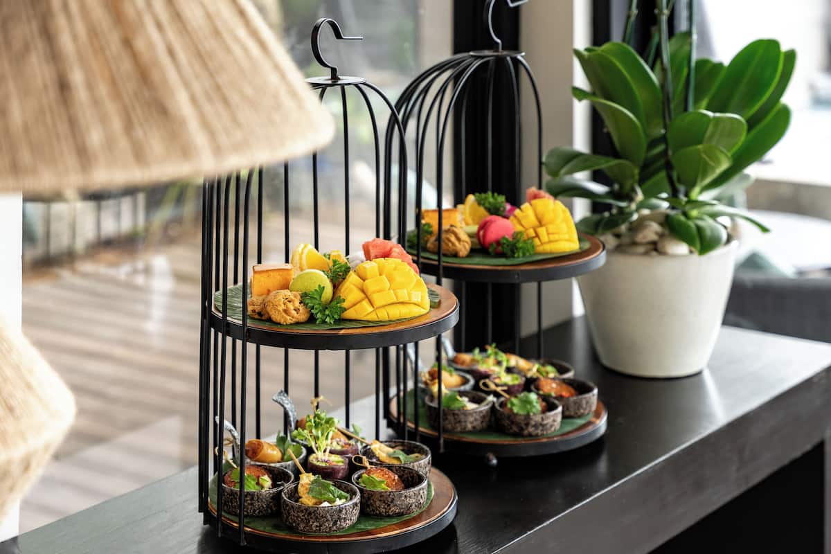 A multi-tiered food display on a table with various dishes, a potted plant, and a lamp.
