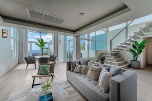 Un salón amplio con sofá, sillas, una mesa de comedor y grandes ventanales con vistas al océano.