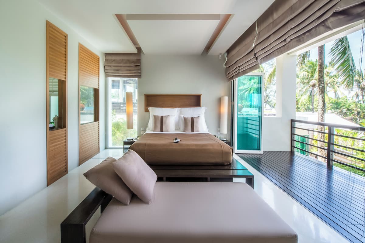 A modern bedroom with a bed, bedside tables, and a balcony with a view of palm trees.
