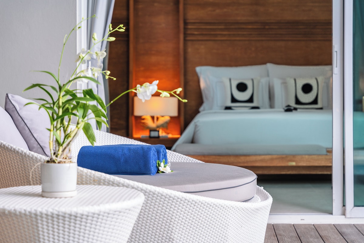 A modern hotel room with a bed, a small table with a plant, and a blue towel.