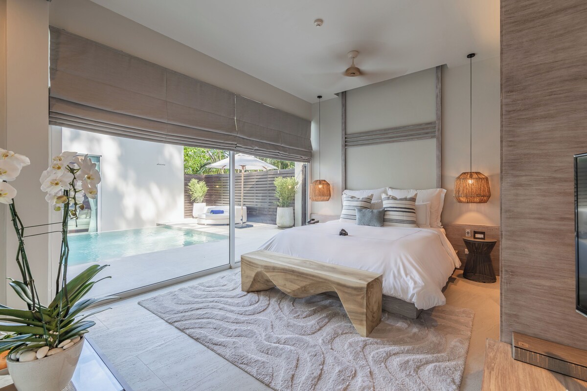 Quarto moderno com uma cama grande, um banco, uma televisão e vista para uma piscina.
